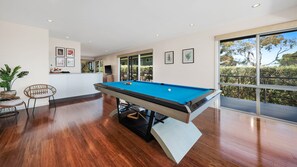 Une table de billard dans une pièce au plancher en bois, avec une chaise et une plante en pot.