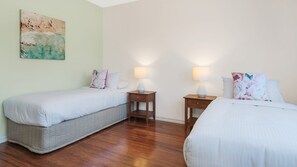 Une chambre d’hôtel avec deux lits simples, un plancher en bois, un tableau au mur et des lampes de chevet.