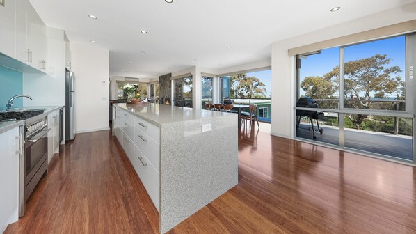 A modern kitchen with a large island, stainless steel appliances, and a dining area with a view.