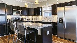 Una cocina moderna con armarios oscuros, electrodomésticos de acero inoxidable y una isla central con taburetes de bar.