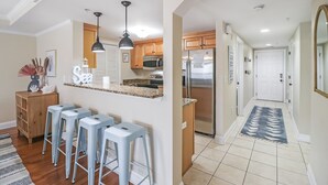 Una cocina moderna con una isla central, taburetes de bar, iluminación colgante y un refrigerador de acero inoxidable.