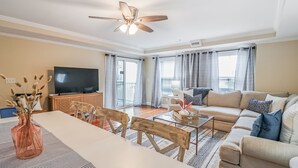 Un salón amplio con un sofá grande, una mesa de comedor con sillas, un televisor y un ventilador de techo.