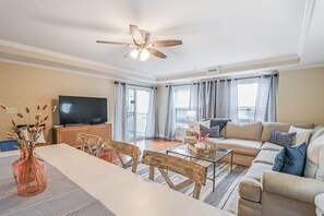 A spacious living room with a large sofa, a dining table with chairs, a TV, and a ceiling fan.