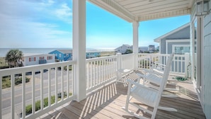 A wooden deck with white railings overlooking a beach.