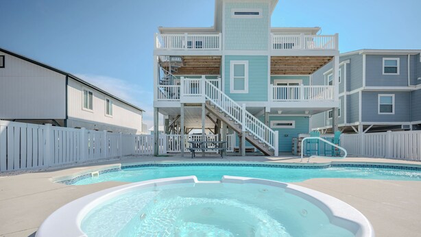 A swimming pool area with a hot tub, a multi-level building with balconies, and a white picket fence.