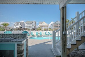 A pool area with a wooden deck, a stone wall, and a view of multiple houses in the background.