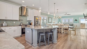 A modern kitchen with white cabinets, a central island with stools, a stainless steel refrigerator, and pendant lighting.