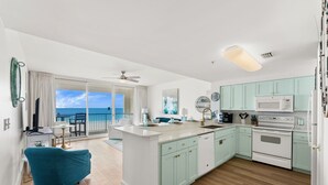 A modern kitchen with light green cabinets, a white island, and a view of the ocean. - Welcome to MAJESTIC-PEARL! Newly renovated in 2026!  
2nd Floor BEACHFRONT! (Panama City Beach)