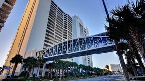 A modern hotel with a pedestrian bridge, palm trees, and high-rise buildings in the background. - Welcome to MAJESTIC-PEARL! Newly renovated in 2026!  
2nd Floor BEACHFRONT! (Panama City Beach)