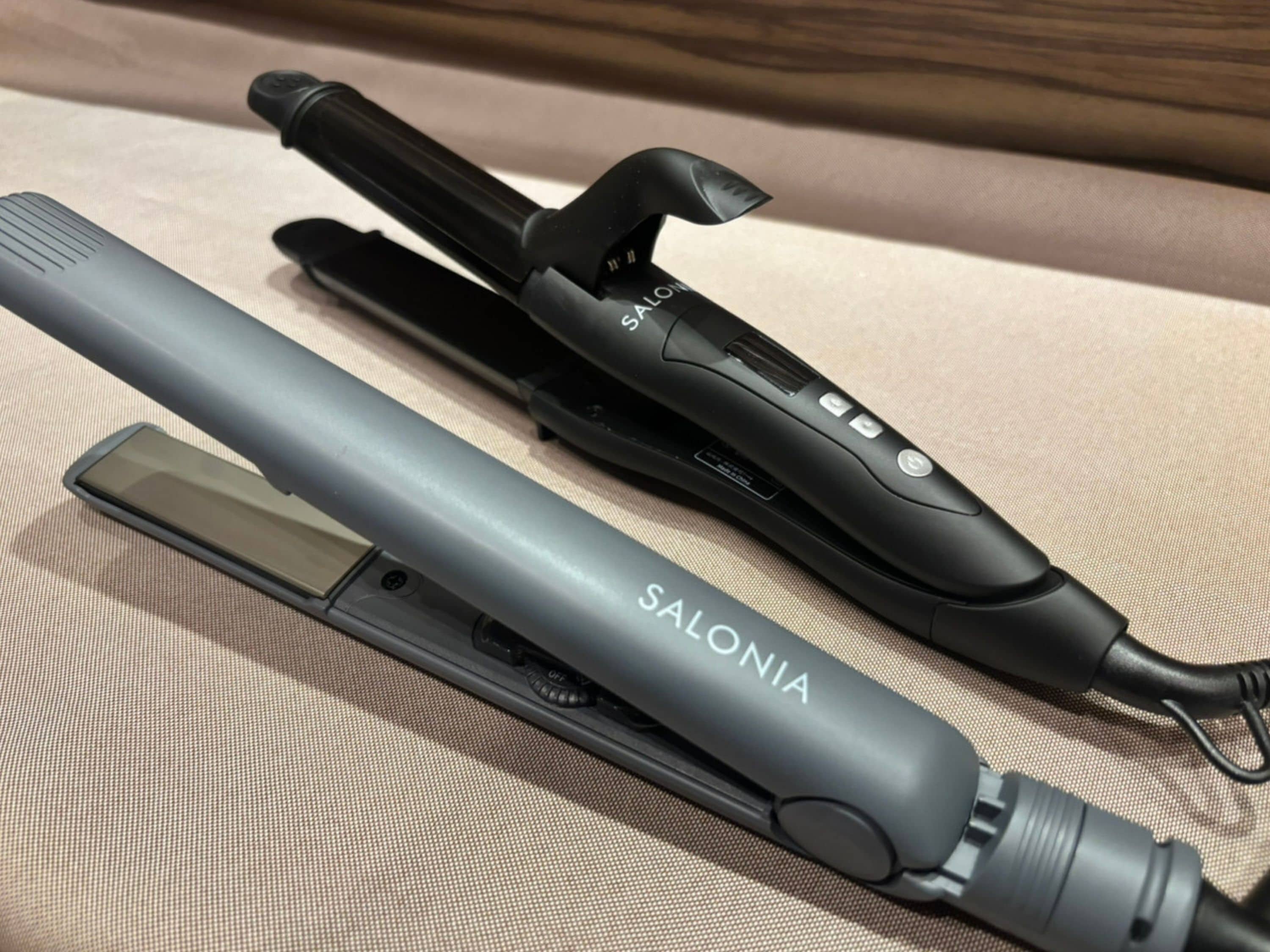 A flat iron and a curling iron on a textured fabric surface.
