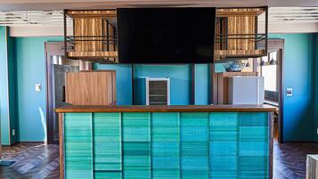 Una zona de bar con televisor de pantalla plana, armarios de madera y mostrador color turquesa.
