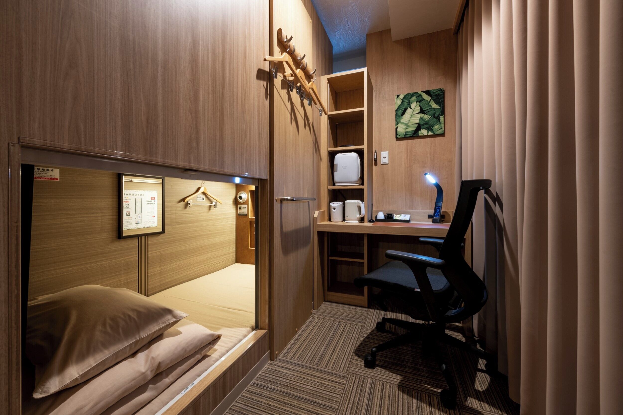 A compact hotel room with a bunk bed, a desk with a chair, a small kitchenette, and a mounted coat rack.