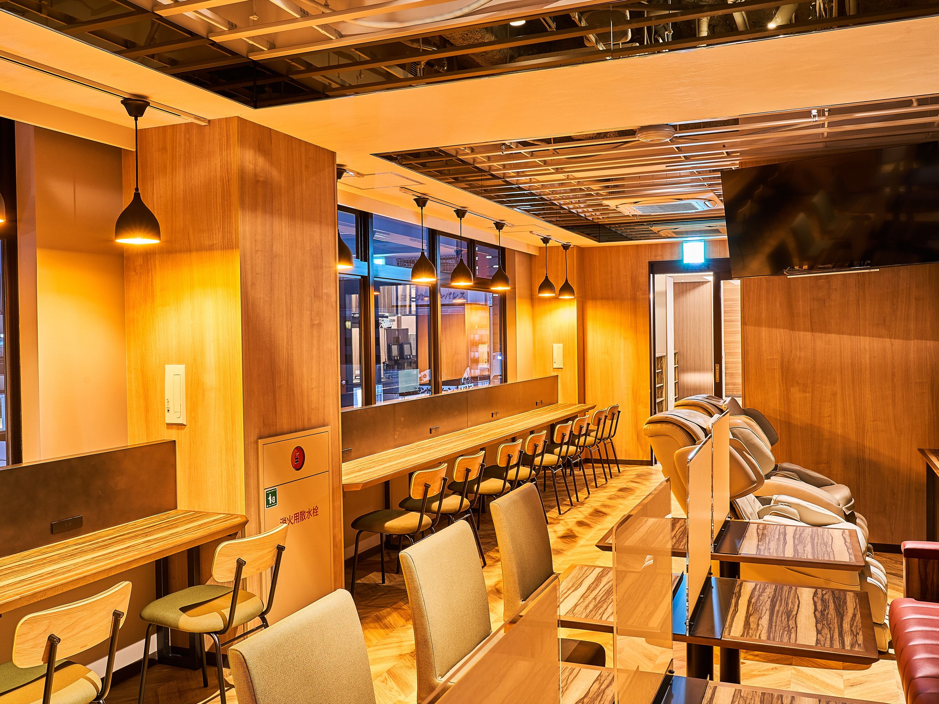 Restaurante moderno com painéis de madeira, iluminação pendente e uma longa mesa comunitária com cadeiras.