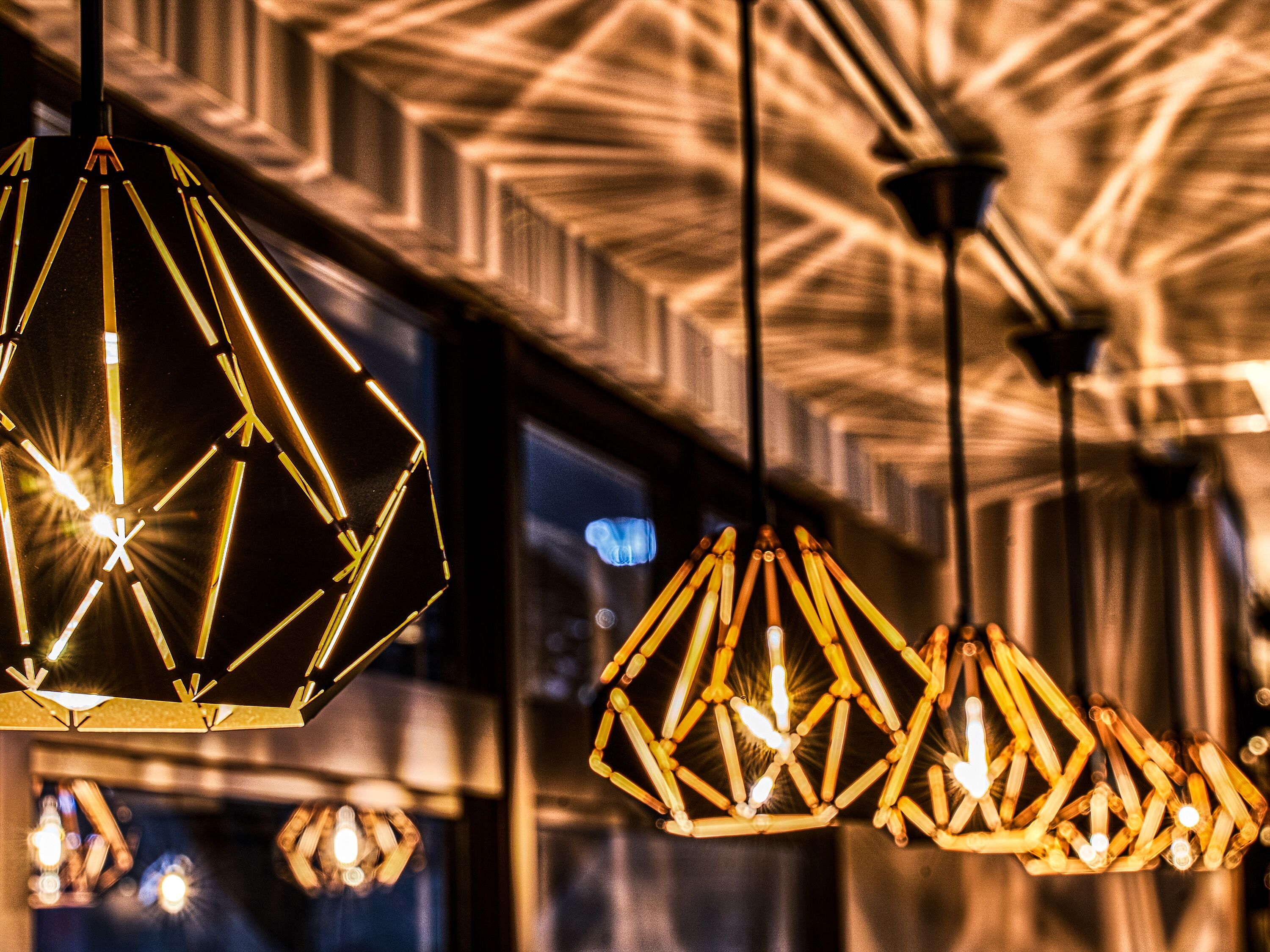 Une série de suspensions géométriques diffusant une lumière chaleureuse, suspendues à un plafond orné de motifs.