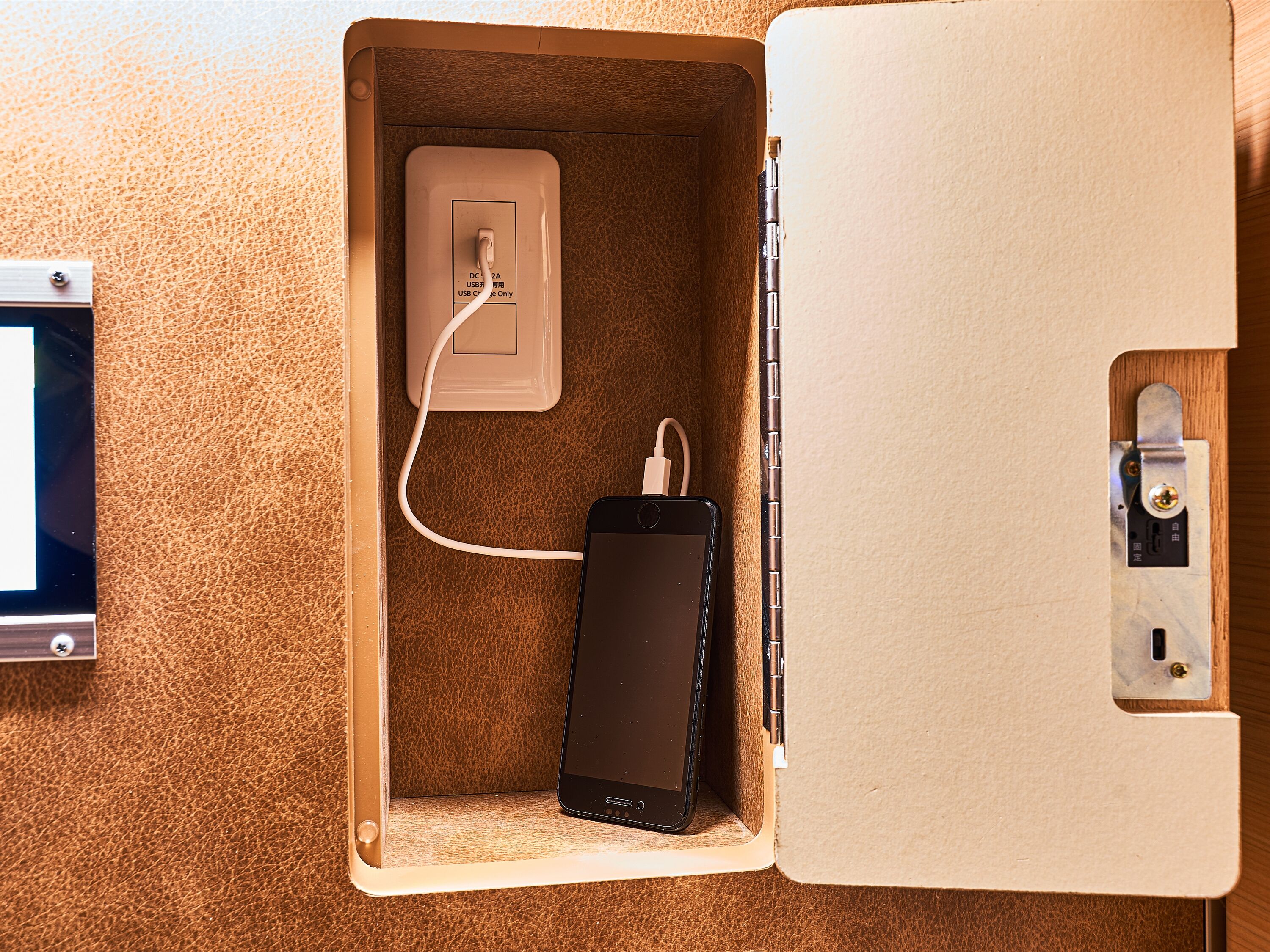 A smartphone charging inside a wooden box with a USB port and a power outlet.