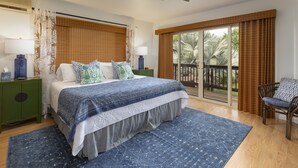 Ein Schlafzimmer mit einem Bett, zwei Nachttischen, einem Deckenventilator, einem großen Fenster mit Vorhängen, einer Schiebetür und einem Sessel.