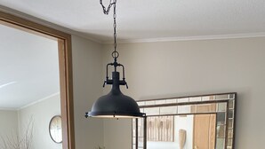 Ein Essbereich mit rundem Tisch, schwarzen Stühlen, einer schwarzen Pendelleuchte, einem Spiegel mit Holzrahmen und einer kleinen Pflanze als Tischdekoration.