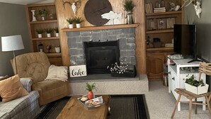 Ein gemütliches Wohnzimmer mit Kamin, Holzregalen, einer Couch und einem Couchtisch.