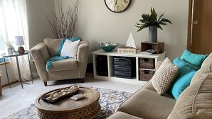 Ein Wohnzimmer mit einer Couch, einem Sessel, einem Couchtisch und einer Uhr an der Wand.