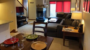 En stue med pejs, sofa, spisebord dækket med tallerkener og glas, og et fjernsyn i baggrunden.