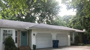 A single-story house with a front porch, two garage doors, and a gravel driveway.