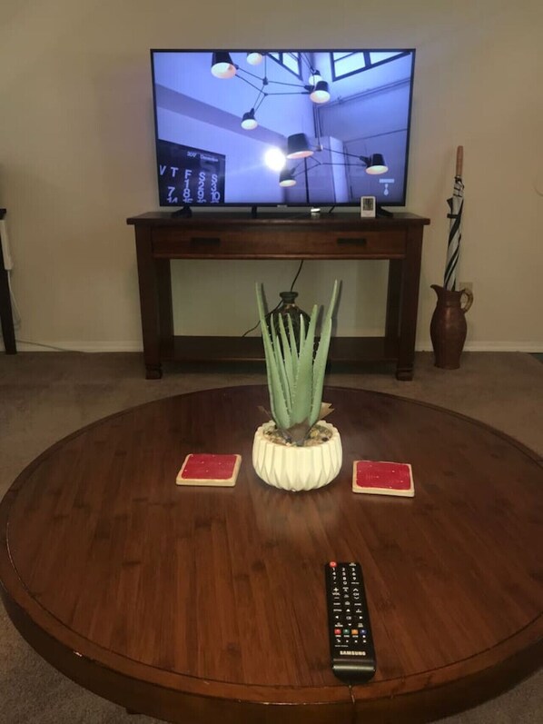 A round wooden coffee table with a cactus centerpiece, two red placemats, a remote control, and a television above a wooden console table. - The Southwest Place 2203 (Ozark)