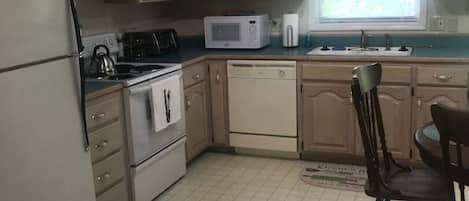 A compact kitchen with wooden cabinets, a microwave, a stove, and a sink.