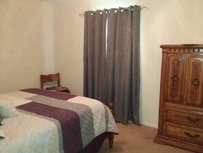 A bedroom with a bed, a wooden dresser, a chair, and a window with curtains. - The Southwest Place 2203 (Ozark)