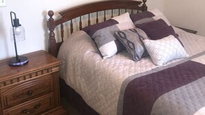 A bedroom with a wooden bed, a nightstand, a lamp, and a painting on the wall.
