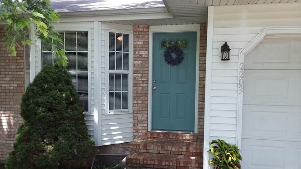 A house with a green door, a welcome mat, and a potted plant.