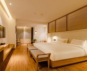 A modern hotel room with a large bed, wooden flooring, a TV, and a bedside table.
