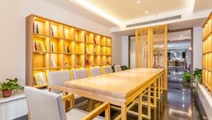 A modern interior with a long wooden table and white chairs, surrounded by illuminated bookshelves.