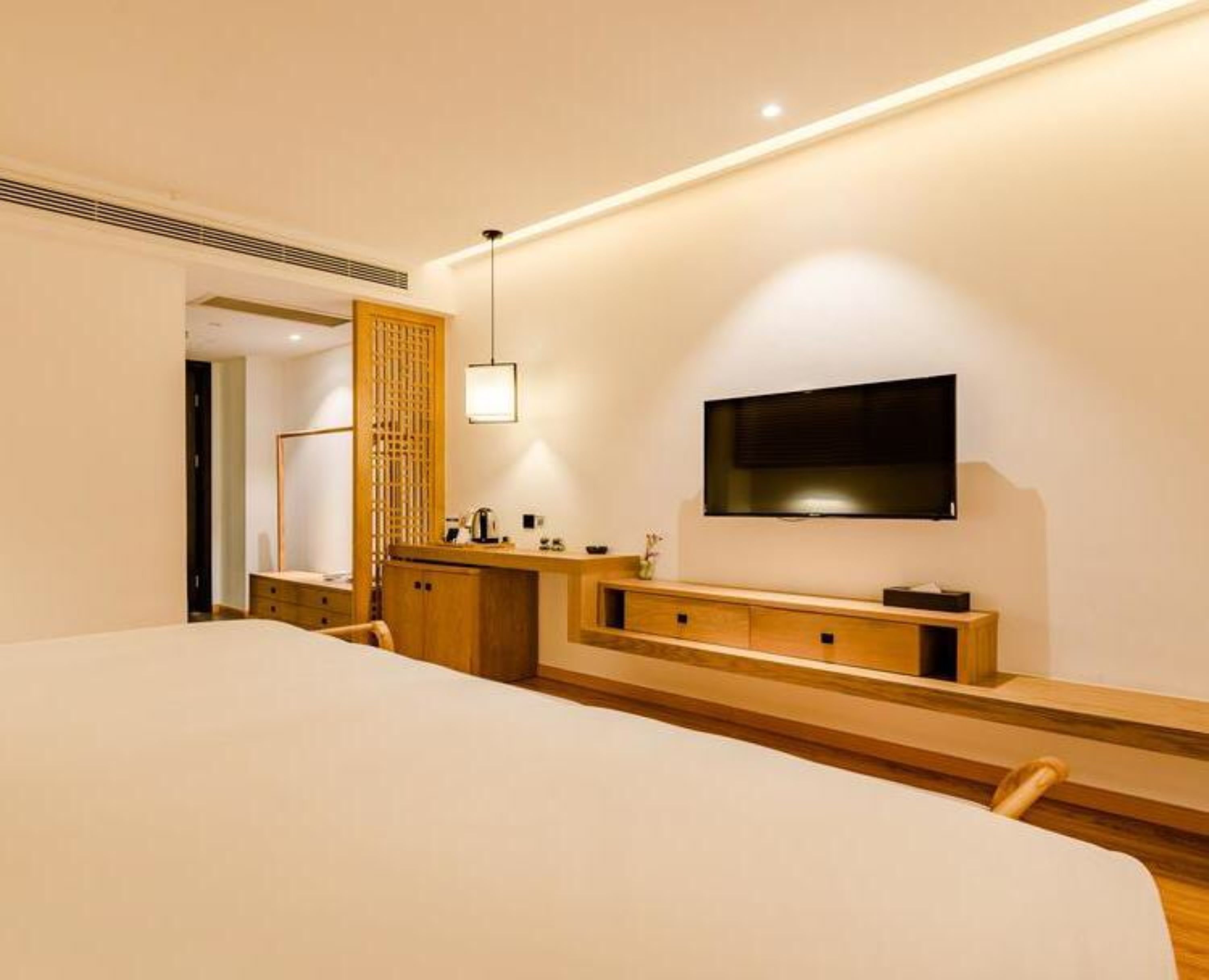 Quarto de hotel moderno com uma cama grande, cómoda de madeira, televisão de tela plana na parede e uma pequena área de trabalho.