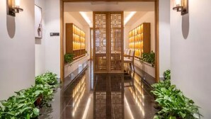 A hallway with a wooden door, potted plants, and wall-mounted lighting fixtures.