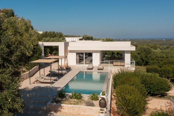 A modern house with a swimming pool, outdoor seating, and a view of the surrounding landscape.