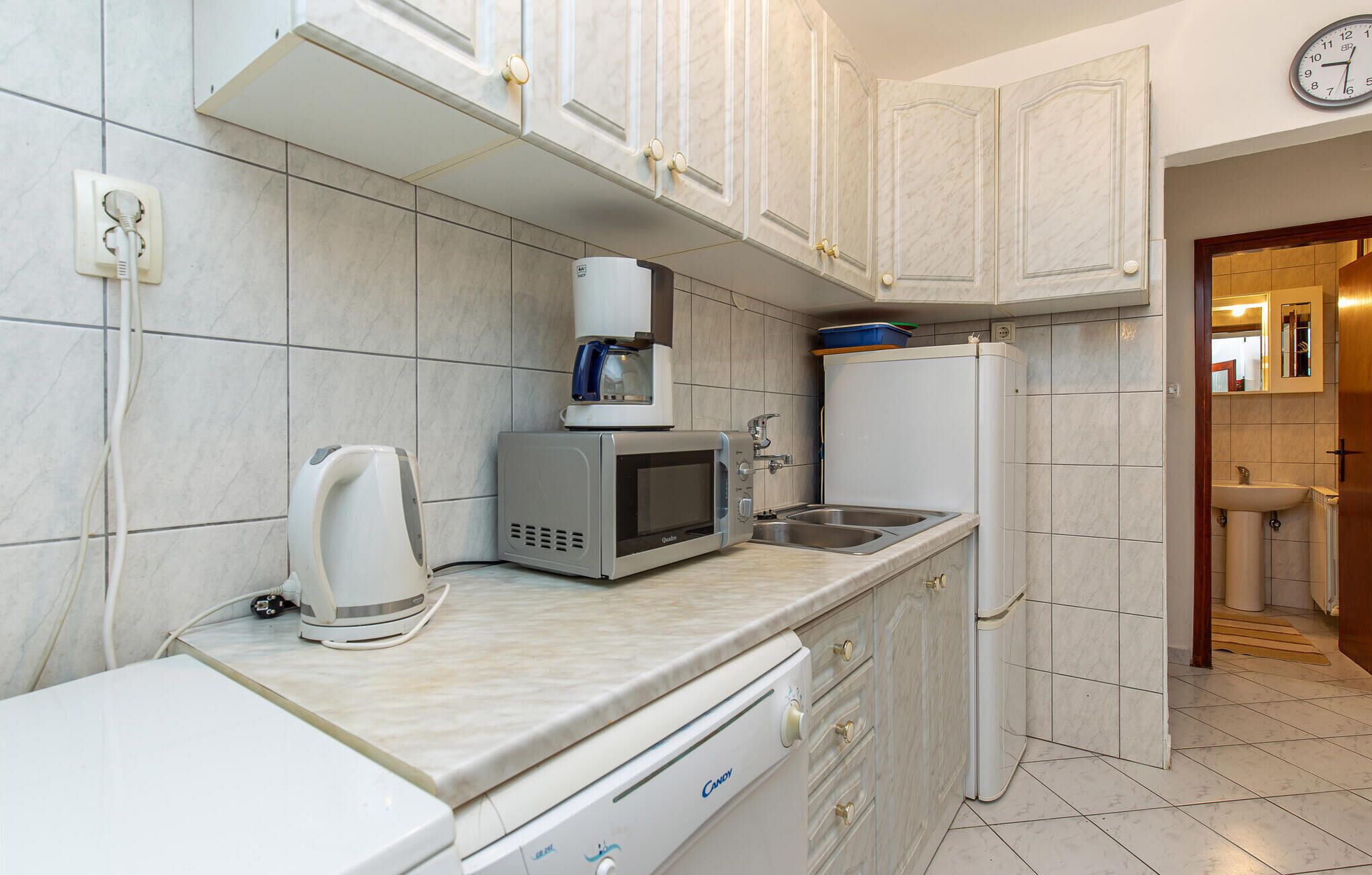 A compact kitchen with white cabinets, a microwave, a kettle, and a refrigerator.