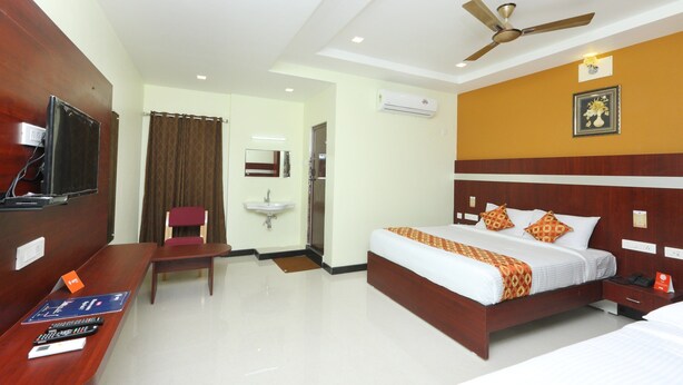 Quarto de hotel com cama, escrivaninha com televisão, cadeira, pia e ventilador de teto.