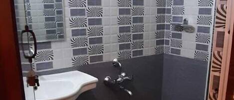 Un baño con cabina de ducha de vidrio, lavamanos y azulejos estampados.