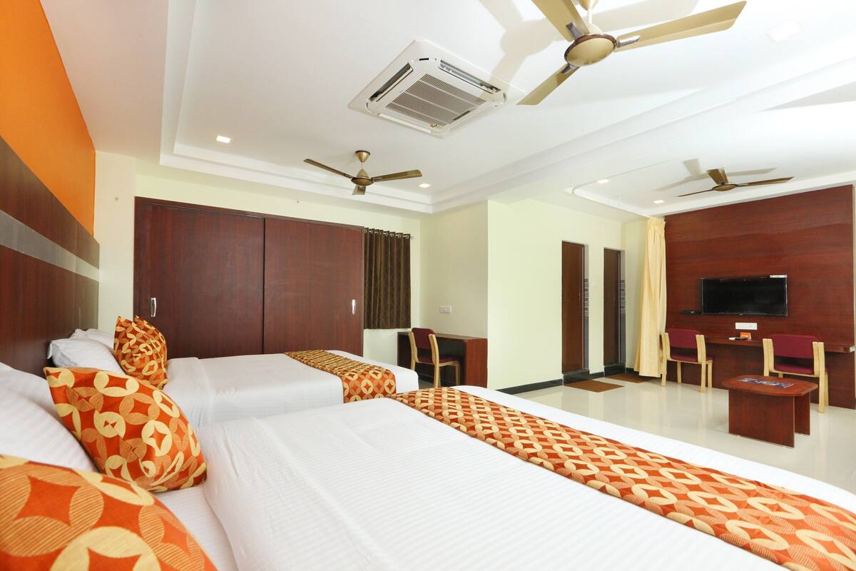 A hotel room with two beds, a TV, a desk, and ceiling fans.