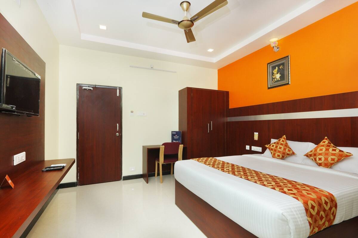 A hotel room with a bed, a desk, a chair, a television, and a ceiling fan.