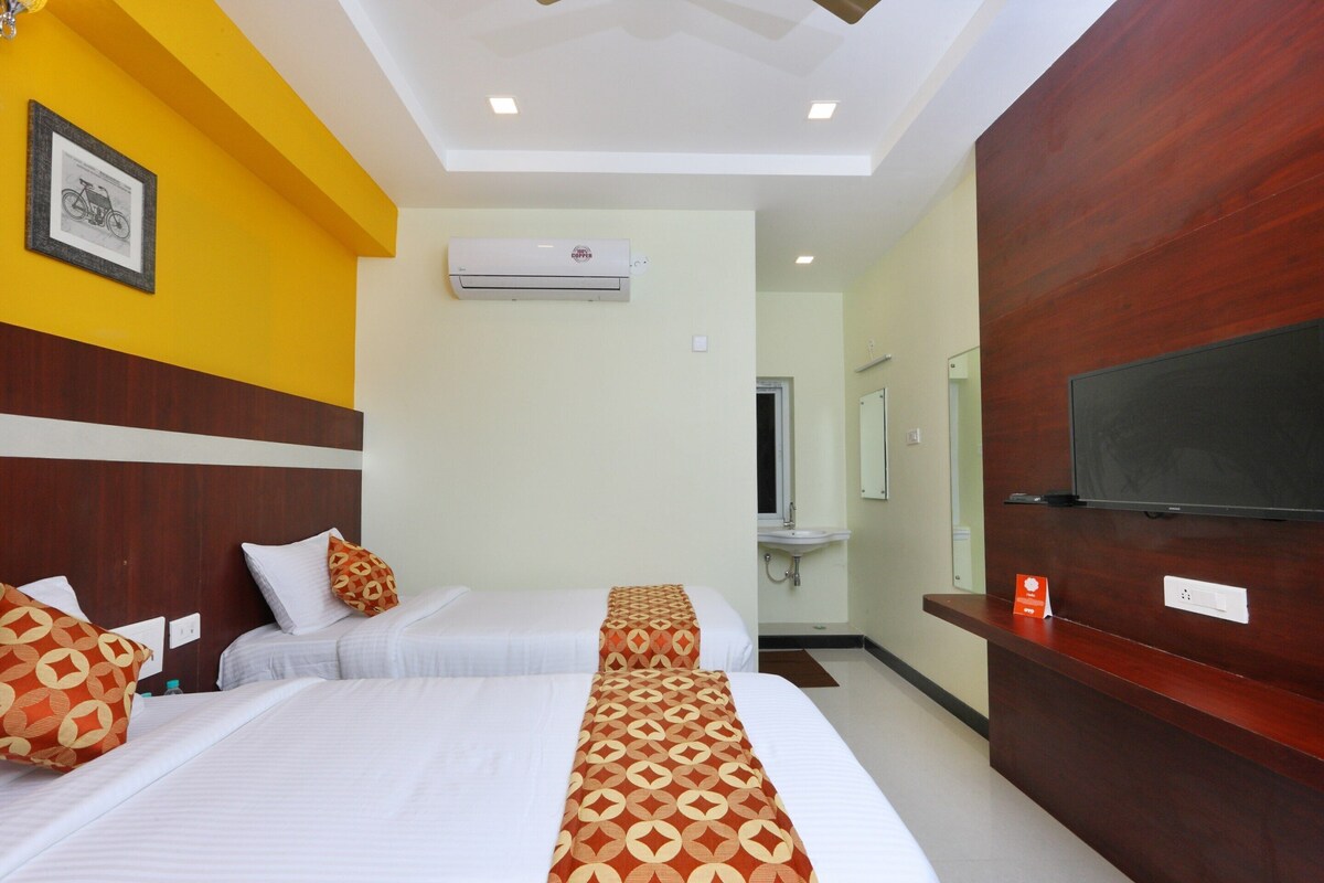 Habitación de hotel con dos camas, un televisor, un espejo y un mostrador de recepción.