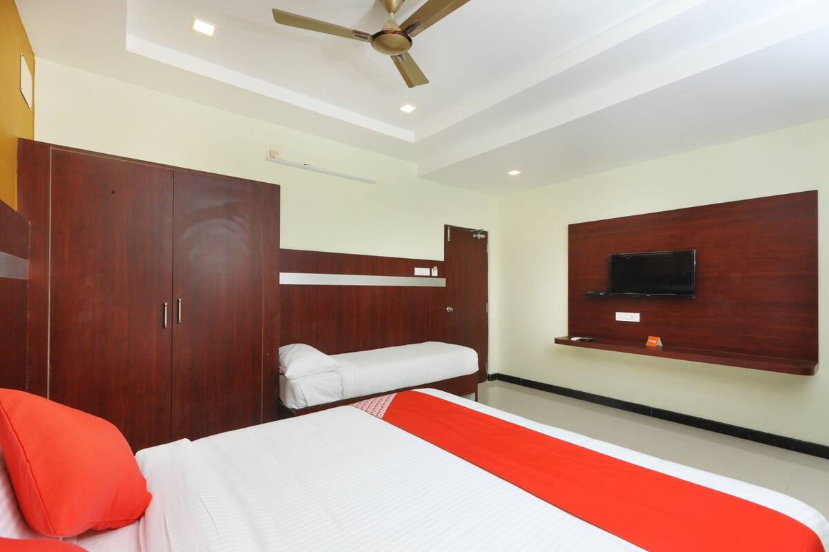 A hotel room with a bed, a wardrobe, a ceiling fan, and a mounted TV.
