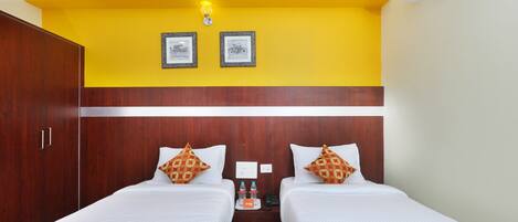 A hotel room with two beds, a wooden wardrobe, a nightstand with a phone and water bottles, and a yellow accent wall.