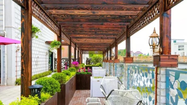 Un espacio de estar al aire libre cubierto, con vigas de madera, macetas con plantas y vistas del paisaje urbano.