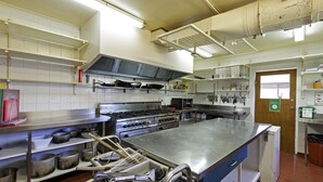 Une cuisine professionnelle équipée d’appareils en acier inoxydable, d’étagères remplies de casseroles et de poêles, et dotée d’un grand îlot central.