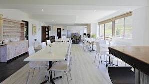 Une cuisine spacieuse et moderne, dotée d’une longue table à manger, de chaises blanches et d’un plan de travail en bois.