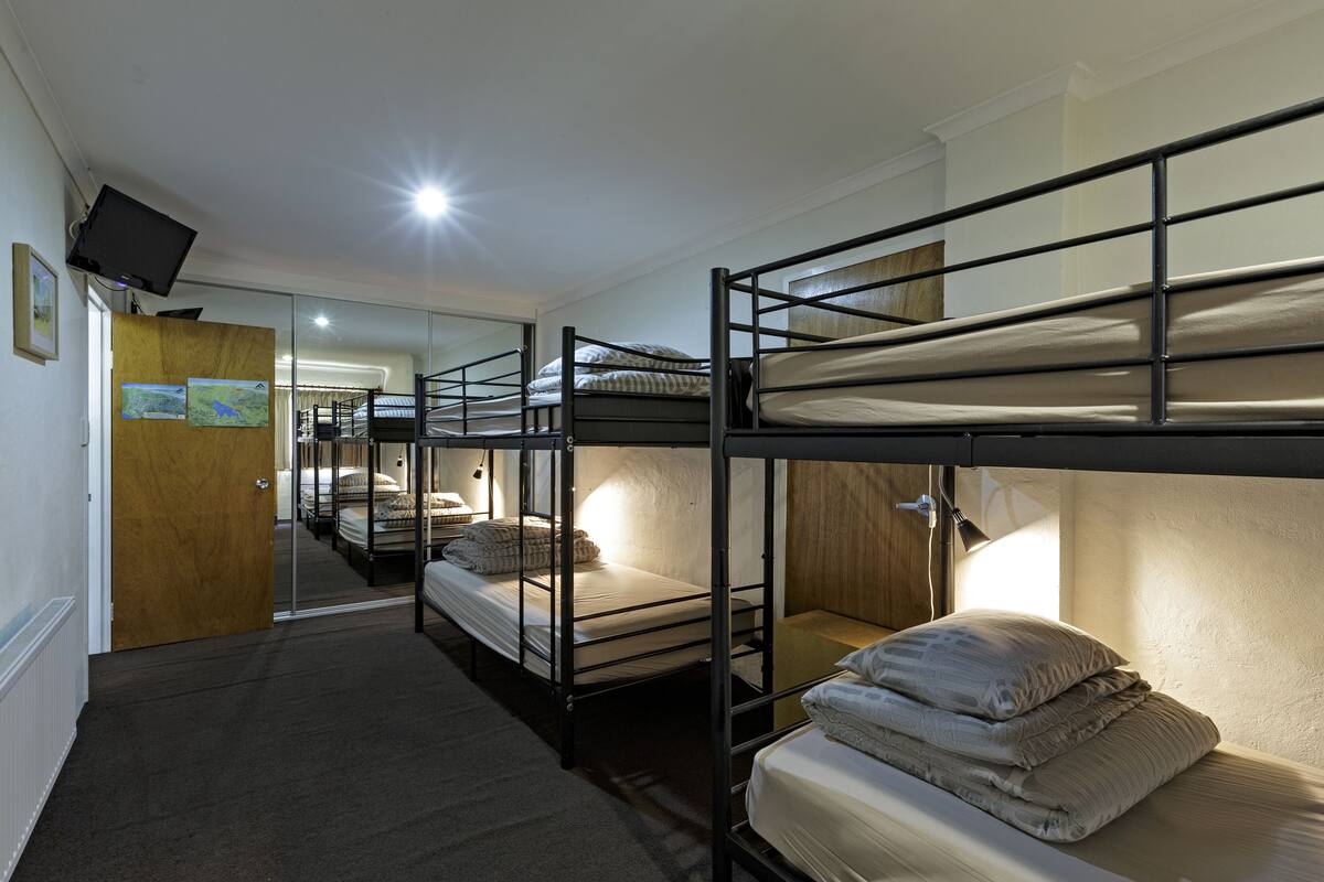 A dormitory room with bunk beds, a wooden door, a television, and a mirror.
