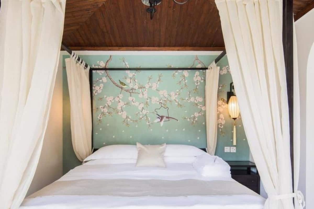 Una cama con sábanas blancas, dosel y pared con papel tapiz floral.