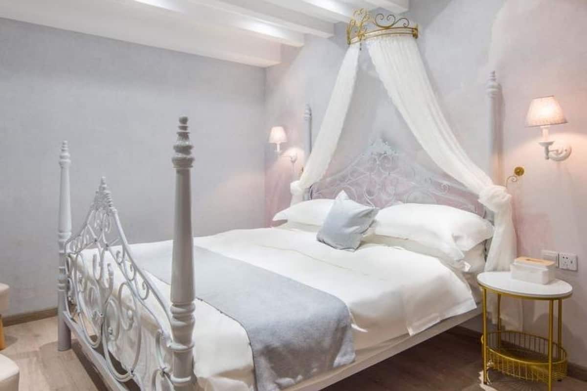 Un dormitorio con una cama con dosel, dos lámparas de noche y una mesita redonda con una bandeja.