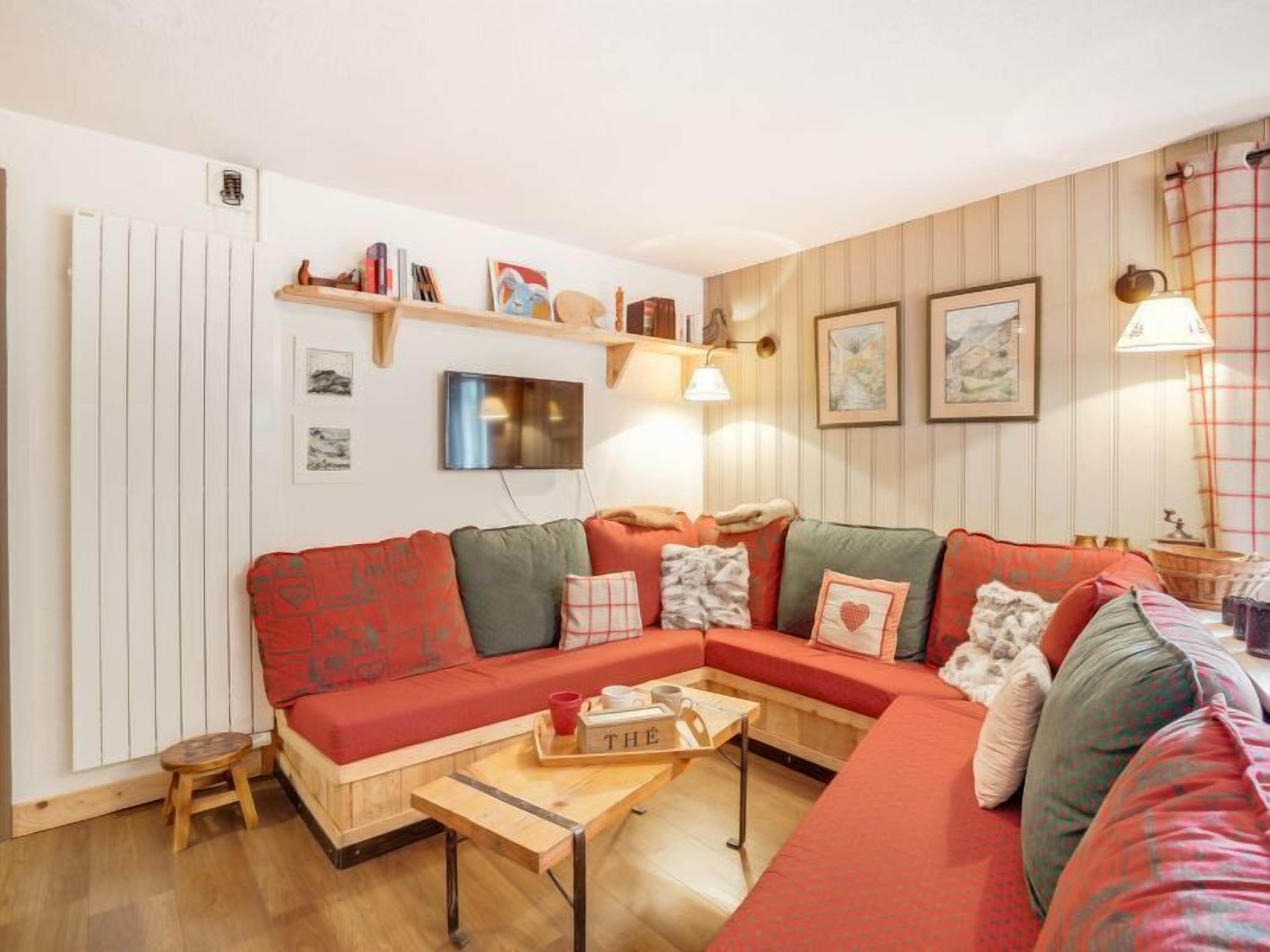 A cozy living room with a sectional sofa, a small wooden coffee table, and a TV mounted on the wall.
